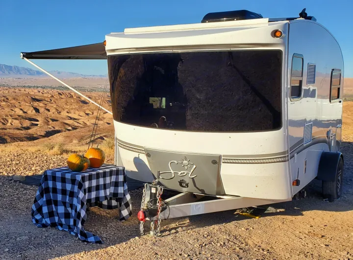 Enjoying an RV rental adventure! A white travel trailer with an awning open, set in a vast desert vista, adorned with fall pumpkins.. InTech RV Sol Horizon 2020