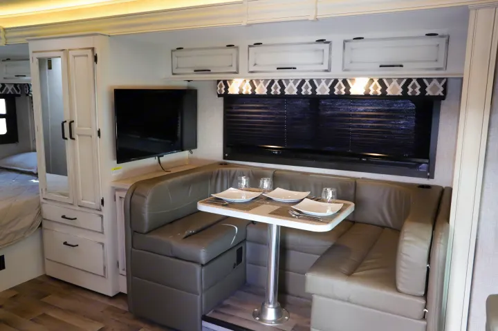 Modern RV rental interior with a cozy dinette, wall-mounted TV, and mirrored wardrobe, offering home-like comfort.. Entegra 24B 2022
