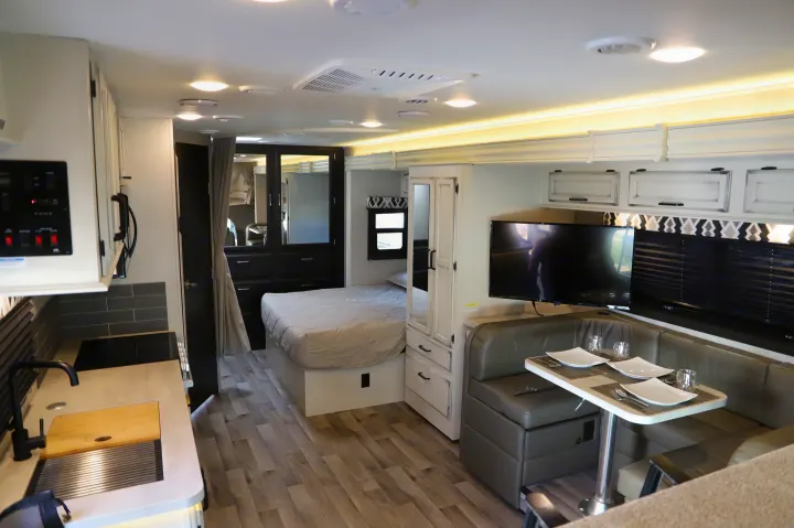 Inside a modern rv rental: kitchen, bedroom, and dining booth with TV, offering comfort for your journey.. Entegra 24B 2022