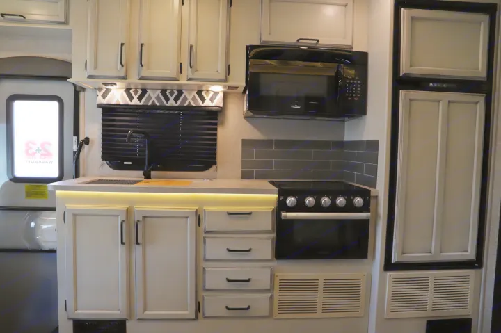 Well-equipped RV rental kitchen featuring light cabinets, black appliances, under-cabinet lighting, and subway tile backsplash.. Entegra 24B 2022