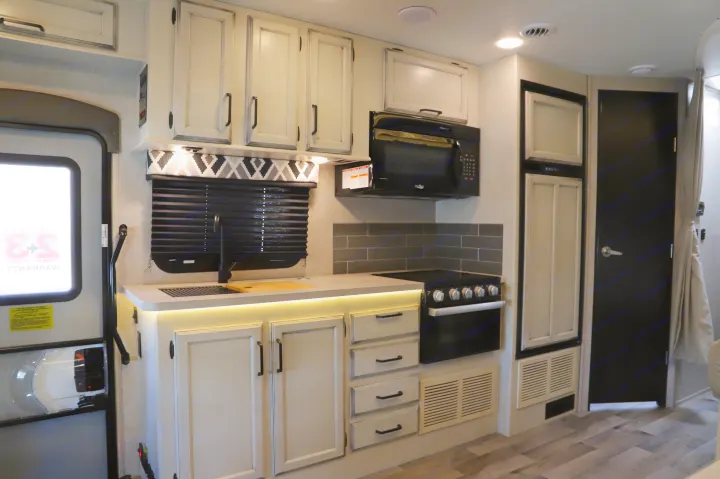 Modern RV rental kitchen interior featuring white cabinets, black appliances, and ample counter space.. Entegra 24B 2022
