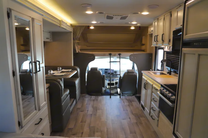 Inside a modern rv rental, showing the full interior layout: kitchen, dining area, and front bunk above the driver's cab.. Entegra 24B 2022