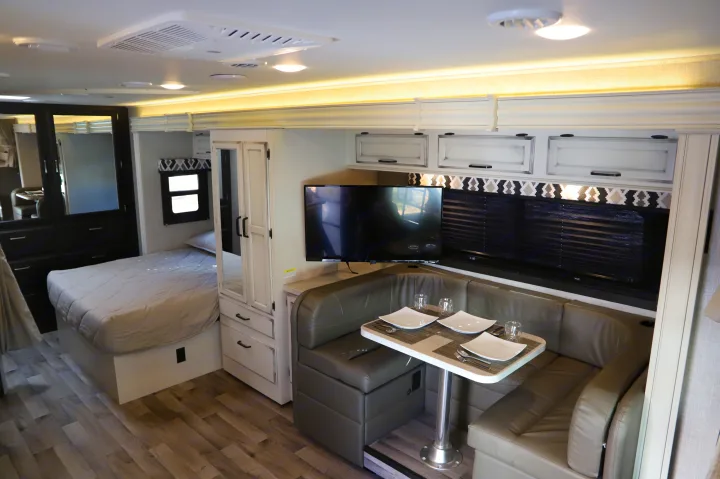 Cozy RV rental interior with bedroom, U-shaped dining booth, flat-screen TV, and modern amenities for comfortable travel.. Entegra 24B 2022