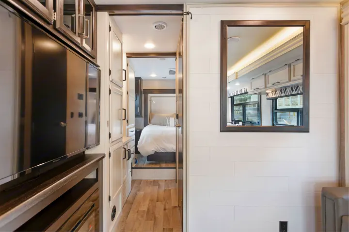 A bright RV rental interior showing a comfortable bedroom, living area with a large mirror, and functional storage space.. Other Other 2022