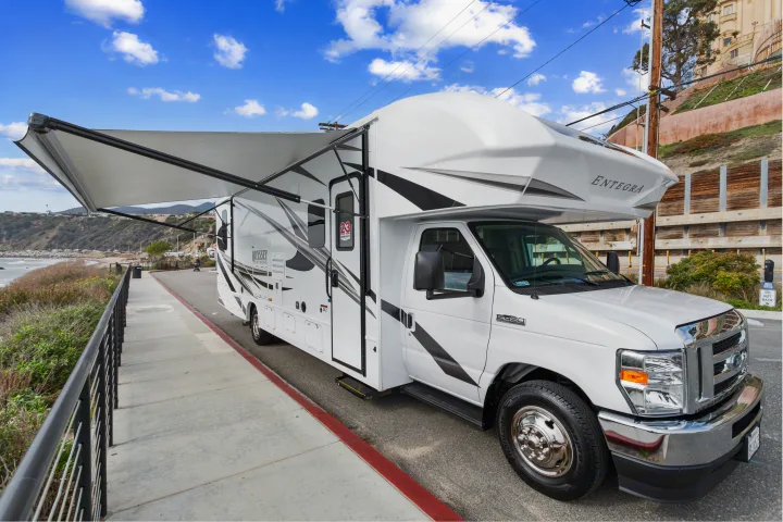 White Class C RV rental parked on a scenic coastal road with an extended awning, overlooking the ocean.. Other Other 2022