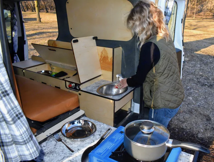 RV rental camper van: A woman washes hands at its compact sink, showcasing the portable kitchen for outdoor living.. Dodge Promaster City 2020