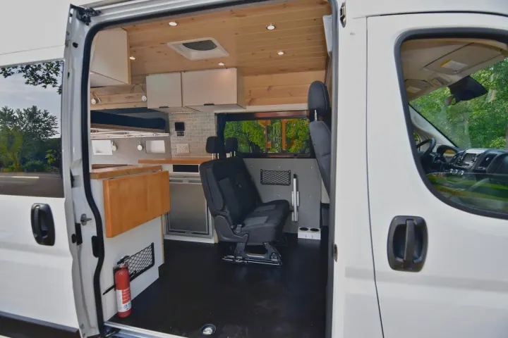 Inviting RV rental camper van interior: wood ceiling, kitchenette, passenger seating, and fire extinguisher near entrance.. Dodge Dodge Promaster 2500 2021