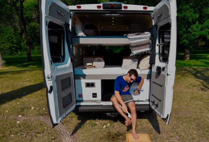 Man washes feet at an RV rental, parked outdoors. Interior shows comfortable bunk beds & smart storage.. Dodge Dodge Promaster 2500 2021