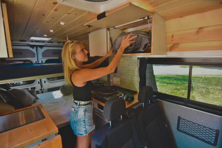 Woman storing items in an RV rental. Features a spacious camper van interior with kitchen, bed, and smart storage.. Dodge Dodge Promaster 2500 2021