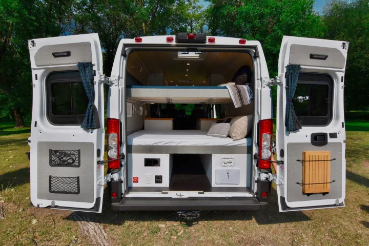 An RV rental's rear doors reveal a bunk bed setup, storage nets, and power access, perfect for road trip adventures.. Dodge Dodge Promaster 2500 2021