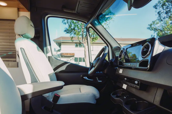 Luxury RV rental interior with bright driver's seat, Mercedes-Benz dashboard, and sunlit outdoor view.. Forest River Coachmen Galleria 2021