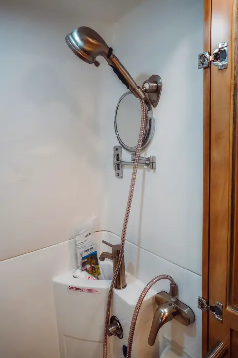 Inside a compact RV rental bathroom, showing a shower, sink, adjustable mirror, and various controls.. Forest River Coachmen Galleria 2021