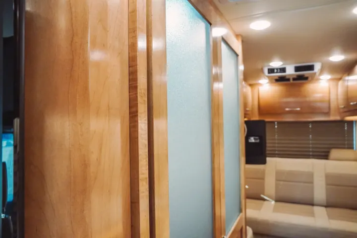 Bright RV rental interior: light wood panels, frosted glass partition, and a beige seating area with overhead cabinets.. Forest River Coachmen Galleria 2021