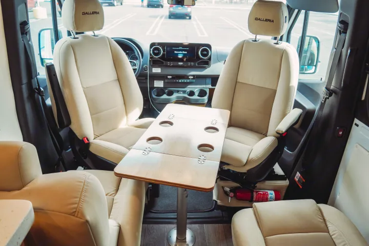 Spacious RV rental interior: cream swiveling front seats, a central table with cup holders, and a Mercedes-Benz dashboard for comfort.. Forest River Coachmen Galleria 2021