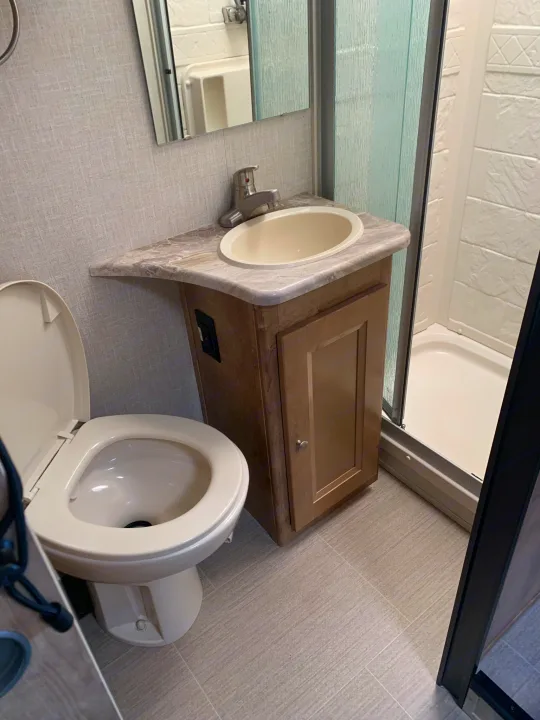 This compact RV rental bathroom includes a toilet, sink with vanity, and shower stall for convenient travel.. Forest River Coachmen Leprechaun 2019