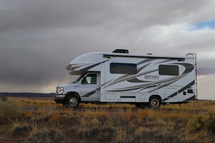 White RV rental on a roadside with dry grass, under a vast, dramatic cloudy sky.. Entegra Coach Odyssey 2021