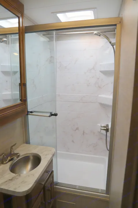 Modern RV rental bathroom: a shower with marbled walls, shelving, and a sleek vanity with a sink.. Entegra Coach Odyssey 2021