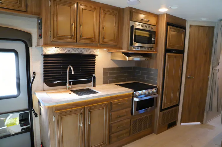 Modern RV rental kitchen showcasing wood cabinets, stainless steel stove, microwave, fridge, and sink. Functional and stylish.. Entegra Coach Odyssey 2021