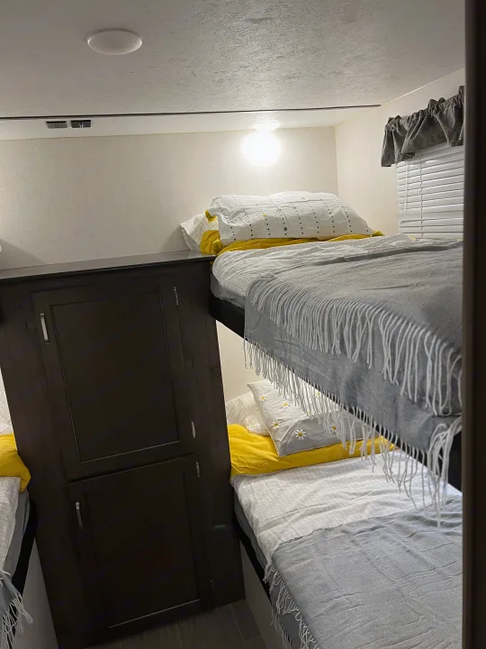 This RV rental features cozy bunk beds with yellow & white bedding, a light fixture, and dark wood storage cabinetry.. Keystone RV Passport SL 2020