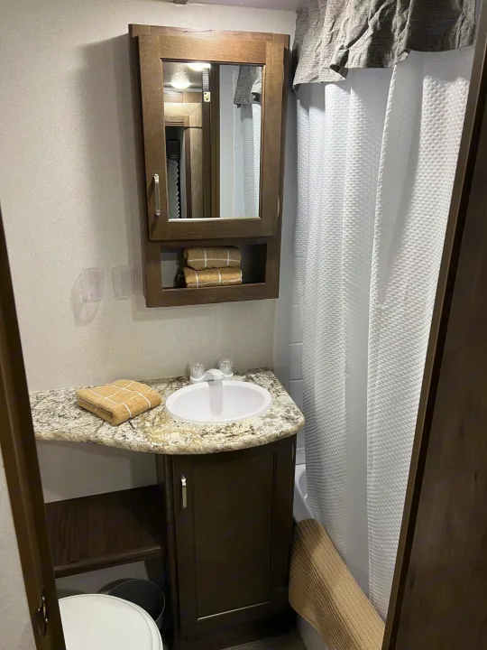 Compact RV rental bathroom featuring a vanity with sink, mirrored cabinet, shower with white curtain, and toilet.. Keystone RV Passport SL 2020