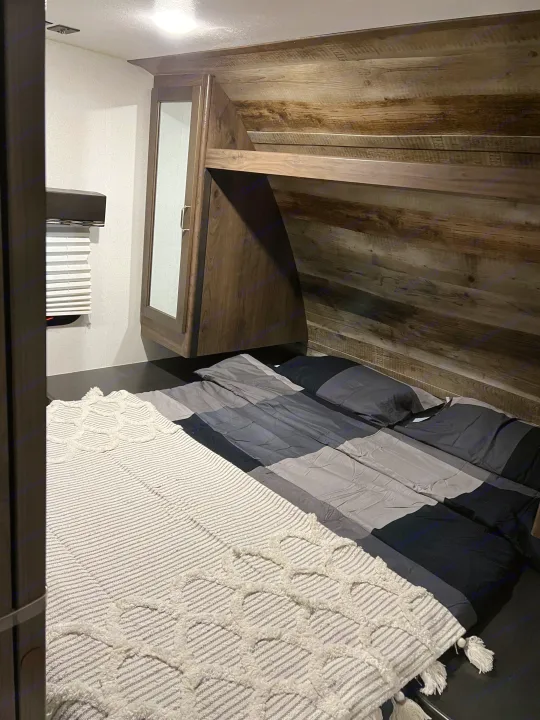 Comfortable RV rental bedroom featuring a modern wooden headboard, soft bedding, and practical overhead storage. Perfect for travel.. Keystone RV Passport SL 2020