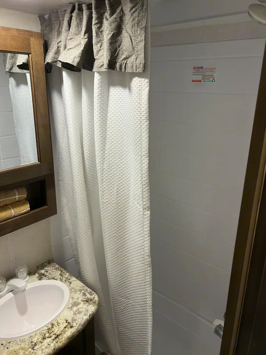 Compact RV rental bathroom featuring a sink, vanity, mirror, and shower with a quilted white curtain. Perfect for travel!. Keystone RV Passport SL 2020