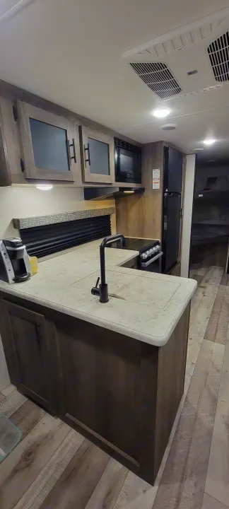 Explore this RV rental's cozy kitchen: a bright space with a large counter, sink, stove, microwave, fridge, and cabinets.. Sportsmen SE 2021