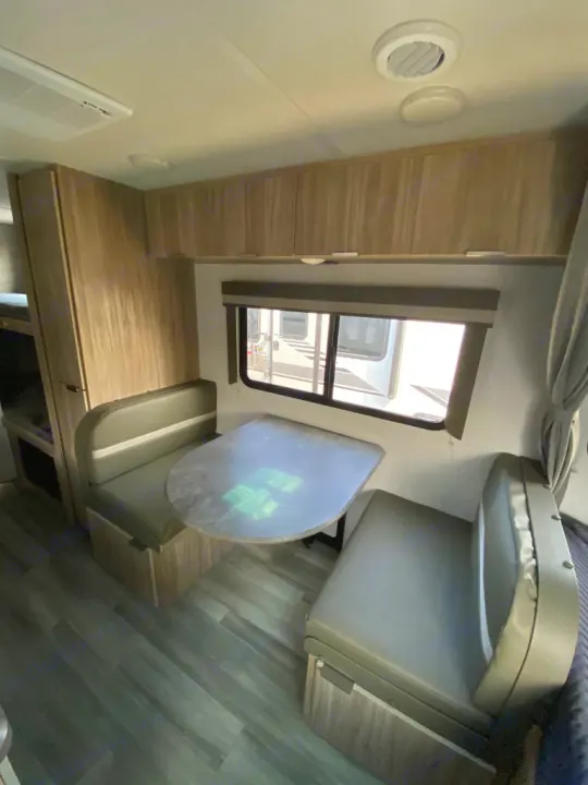 Spacious RV rental dinette with cozy benches, overhead storage, and a large window, perfect for meals & relaxation.. Winnebago Micro Minnie 1800BH 2022