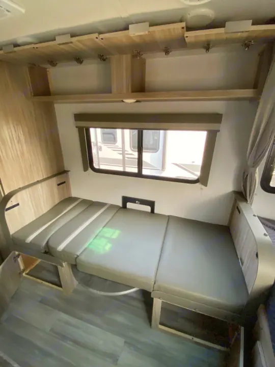 RV rental interior featuring a versatile dinette that converts to a bed, with convenient overhead storage and a bright window.. Winnebago Micro Minnie 1800BH 2022