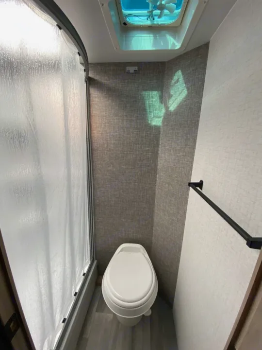 RV rental's compact bathroom: toilet, frosted shower door, and overhead fan. Efficient small space living.. Winnebago Micro Minnie 1800BH 2022