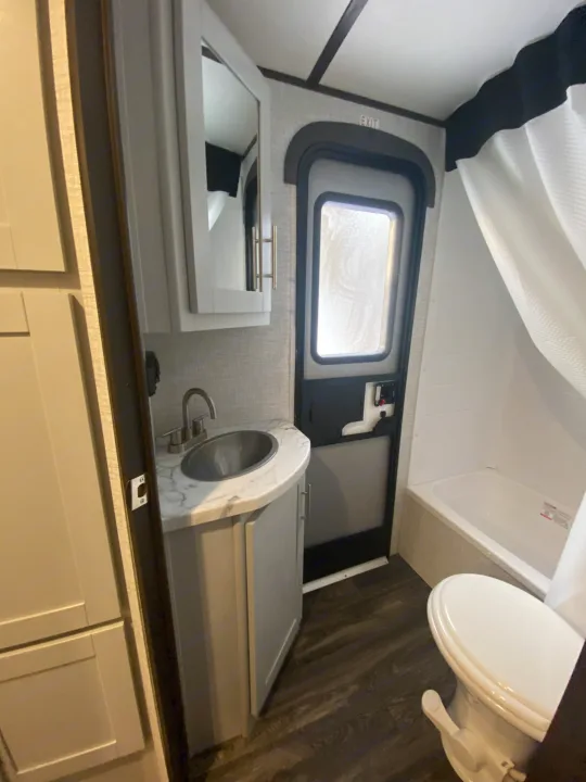 Inside an RV rental: a compact bathroom with a sink, toilet, tub/shower, and the main exit door. Bright and functional.. Keystone RV Bullet Ultra Lite 2021