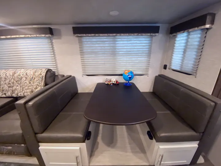 Spacious RV rental dinette with comfortable booth seating, perfect for meals & activities. Features multiple windows with blinds.. Keystone RV Bullet Ultra Lite 2021