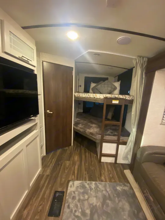 Modern RV rental living area featuring a mounted TV, a door, and cozy bunk beds. Perfect for family adventures.. Keystone RV Bullet Ultra Lite 2021