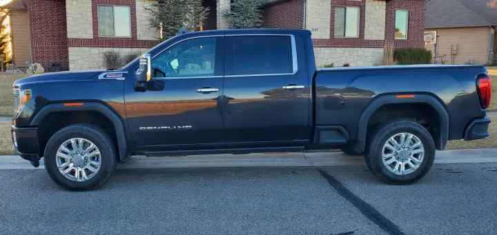 A dark gray GMC Denali HD pickup truck. This heavy-duty vehicle is parked by a brick house, ready for an rv rental tow or adventure.. GMC Sierra 2500HD Denali 2020