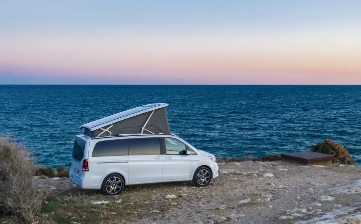 White camper van with pop-top roof by the ocean at sunset. Perfect for your next rv rental adventure by the sea.. Mercedes Marco Polo 2022