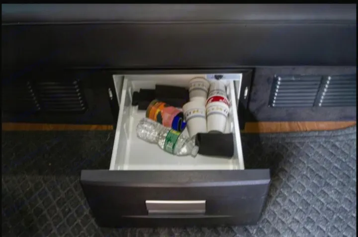 Inside an RV rental, a pull-out mini-fridge drawer reveals a water bottle, mugs, and organizers beneath the seating.. Mercedes-Benz Sprinter 2500 2016