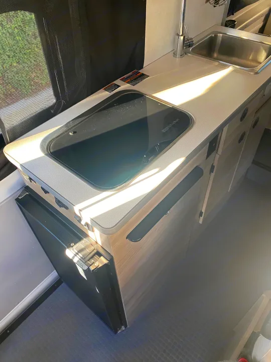 Inside an RV rental: a compact kitchen area with a shiny sink, sleek countertop, and integrated appliances for comfortable travels.. Winnebago Solis 59P 2021