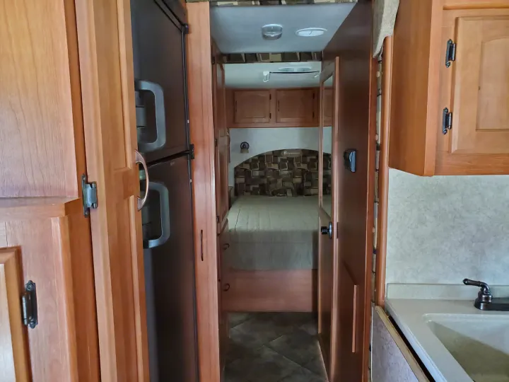 RV rental interior shows a compact kitchen with sink, refrigerator, and a hallway leading to a cozy bedroom.. Adventurer Ford Adventurer RV 2014