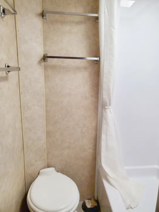 Compact RV rental bathroom with toilet, shower, and towel bars. Features light-colored walls and a shower curtain.. Adventurer Ford Adventurer RV 2014