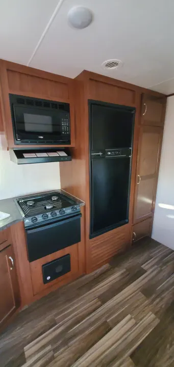 RV rental: A clean kitchen interior featuring a microwave, stove, and refrigerator within wooden cabinetry. Hardwood-style flooring.. Jayco Jay Flight 2017