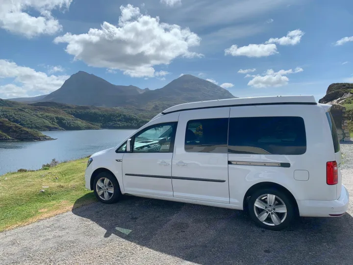 White campervan RV rental by a stunning loch with mountains. Perfect for exploring scenic routes.. Volkswagen Caddy Maxi 2017