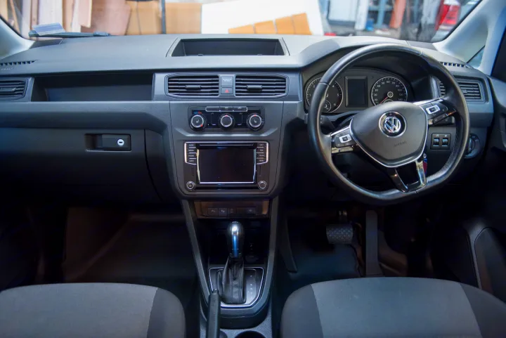 Driver's view of an RV rental's dashboard, with a VW steering wheel, central infotainment screen, climate controls, and automatic gear shift.. Volkswagen Caddy Maxi 2017
