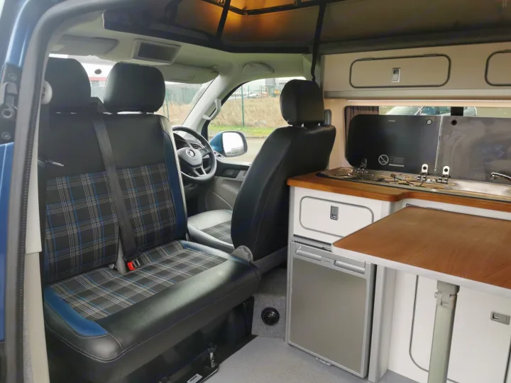 RV rental campervan interior: kitchenette (sink, stove), fridge, plaid seats, and pop-top roof overhead.. Volkswagen T5 2018