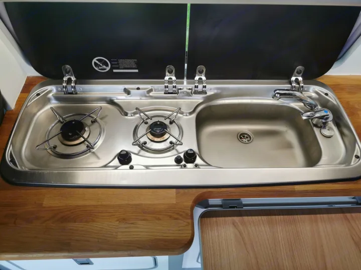 Explore this RV rental's compact kitchen: a two-burner stovetop, integrated sink, and faucet on a wooden countertop.. Volkswagen T5 2018