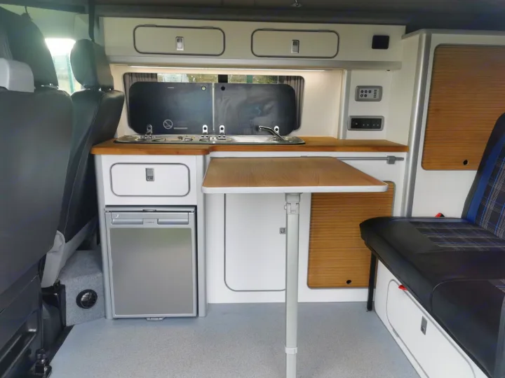 Compact camper van interior with kitchenette, fold-out dining table, fridge, and storage. Ideal for an rv rental adventure.. Volkswagen T5 2018