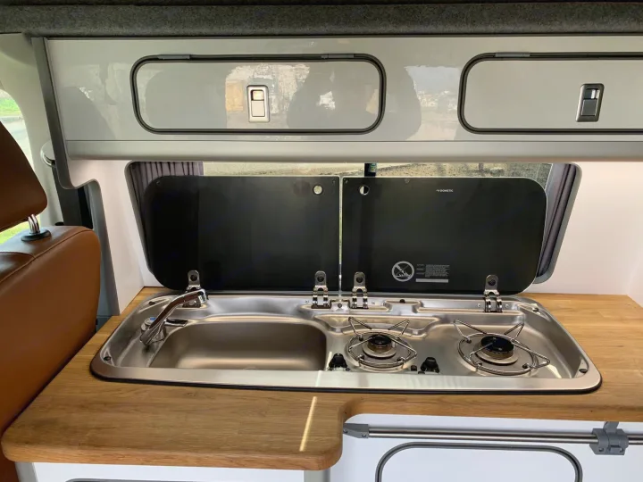 Explore a modern rv rental campervan kitchen: stainless steel sink, Dometic two-burner stove, and overhead storage.. Volkswagen T6 2018