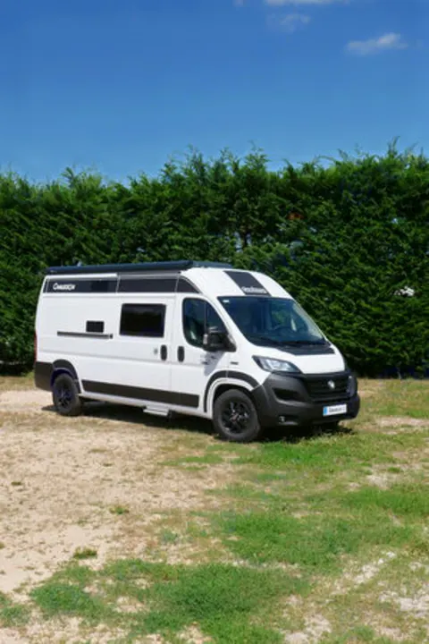 White Chausson camper van RV rental with black accents parked on a sunny day against green hedges.. CI kyros 2023