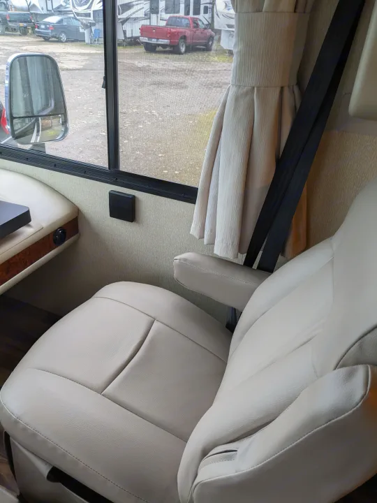 Comfortable beige leather driver's seat in an RV rental, with a window view of other vehicles in an RV park.. Coachmen Pursuit 2017