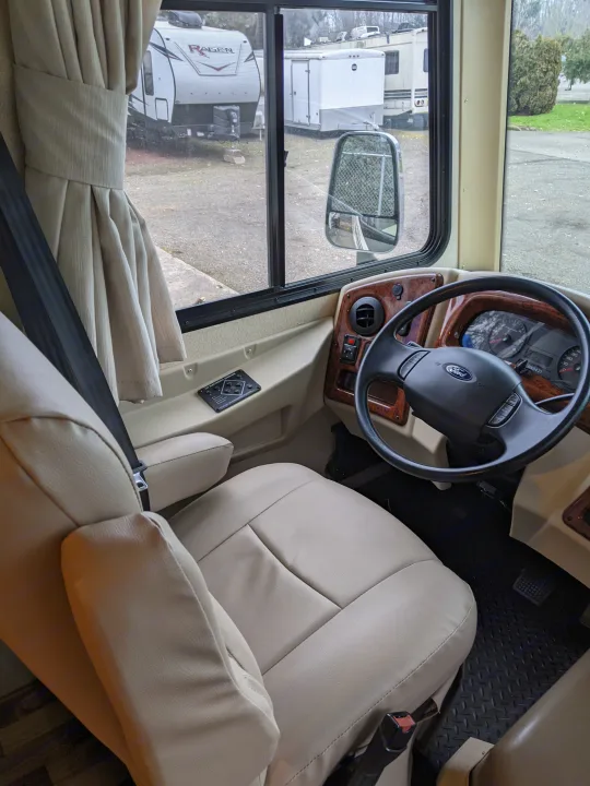 RV rental interior: driver's seat, Ford steering wheel, dashboard, and side window view showing other RVs.. Coachmen Pursuit 2017