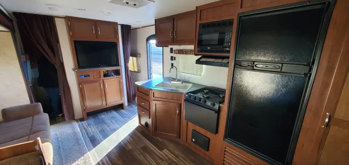 RV rental interior: A full kitchen (sink, stove, microwave, fridge), TV, and seating area in a cozy, brown-toned space.. Jayco Jay Flight 2017